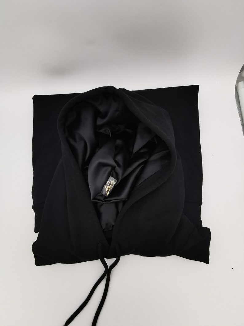 May include: Black hooded sweatshirt with a satin lining. The hood is folded down and the drawstring is visible.
