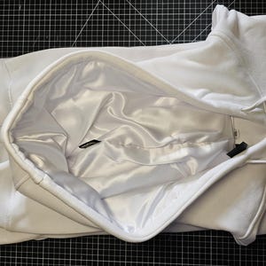 May include: White hooded sweatshirt with a satin lining. The hood is folded back to reveal the lining.