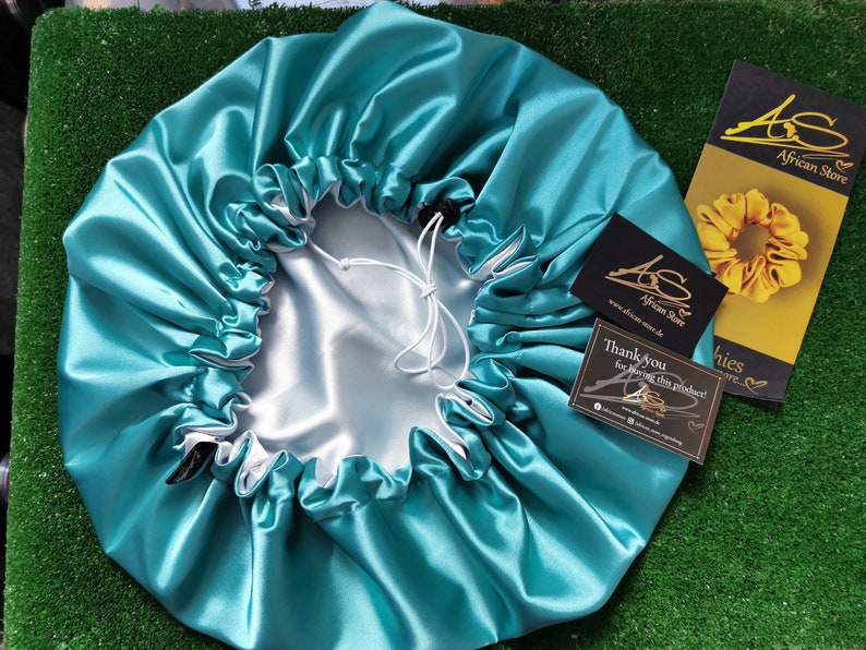 Pu&ograve; includere: Un cappuccio in raso turchese con coulisse bianca e interno grigio chiaro. Il cappuccio &egrave; circondato da biglietti da visita con il testo "AS African Store" e "Thank you for buying this product!"