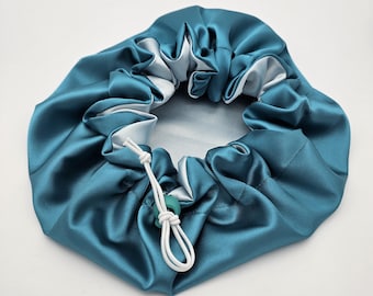Può includere: Un copricapo da notte in raso color teal con un cordoncino bianco e un bottone verde.