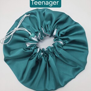 Pu&ograve; includere: Cappello in raso verde acqua con interno bianco e chiusura con coulisse. Il cappello &egrave; progettato per proteggere i capelli durante il sonno. La parola "Teenager" &egrave; visualizzata su un rettangolo verde.