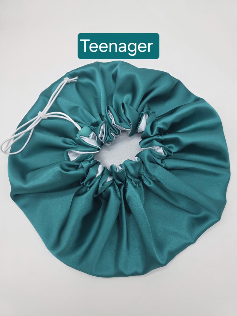 Pu&ograve; includere: Cappello in raso verde acqua con interno bianco e chiusura con coulisse. Il cappello &egrave; progettato per proteggere i capelli durante il sonno. La parola "Teenager" &egrave; visualizzata su un rettangolo verde.