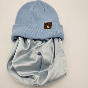 Könnte beinhalten: Eine hellblaue Mütze mit einem braunen Lederflicken, auf dem "Afro Store" in weißen Buchstaben steht. Die Mütze liegt auf einer hellblauen Satin-Schlafhaube.