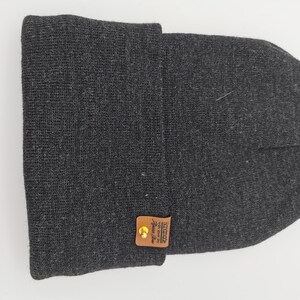 May include: A gray knit beanie with a brown leather patch that says "Unique since 1982" in white text.