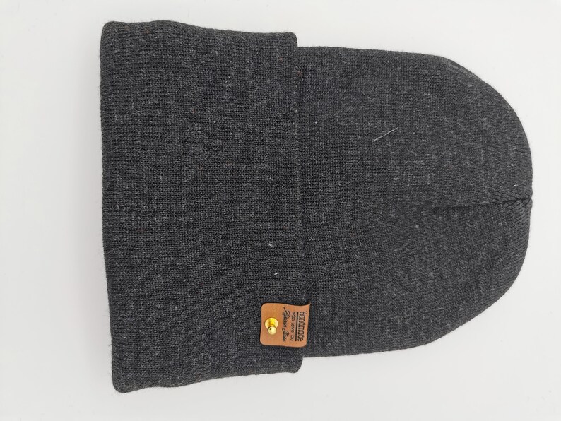 May include: A gray knit beanie with a brown leather patch that says "Unique since 1982" in white text.