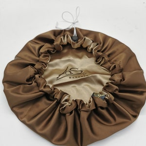 以下が含まれることがあります： ドローストリングクロージャーと「Bonnets by S」という金色のロゴが付いた、茶色のサテン製のヘアボンネットです。
