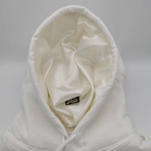 May include: White hooded sweatshirt with a white satin lining and a small black label with gold lettering that says "Signature Brand" inside the hood.
