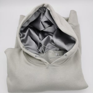 May include: A light gray hooded sweatshirt with a satin lining. The hood is pulled up and the sweatshirt is folded in half.