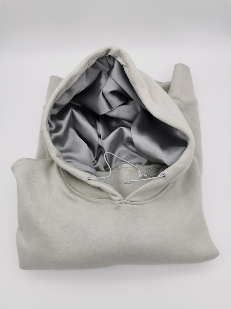 May include: A light gray hooded sweatshirt with a satin lining. The hood is pulled up and the sweatshirt is folded in half.