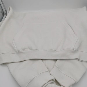 May include: A white hoodie with a pouch pocket on the front. The hoodie is folded in half and the hood is tucked inside.
