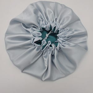 Pu&ograve; includere: Un cappuccio in raso azzurro con interno verde acqua. Il cappuccio &egrave; raccolto nella parte superiore con una chiusura a coulisse. Il tessuto ha una consistenza lucida e liscia. Questo accessorio per capelli &egrave; progettato per proteggere i capelli.