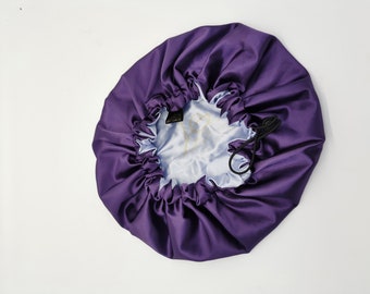 Può includere: Un berretto da notte in raso viola con chiusura a coulisse. Il berretto è foderato con un tessuto in raso blu chiaro.