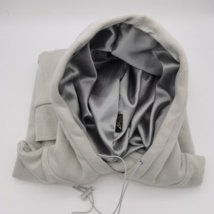 May include: A gray hooded sweatshirt with a silver satin lining. The hood is pulled up and the drawstring is visible.