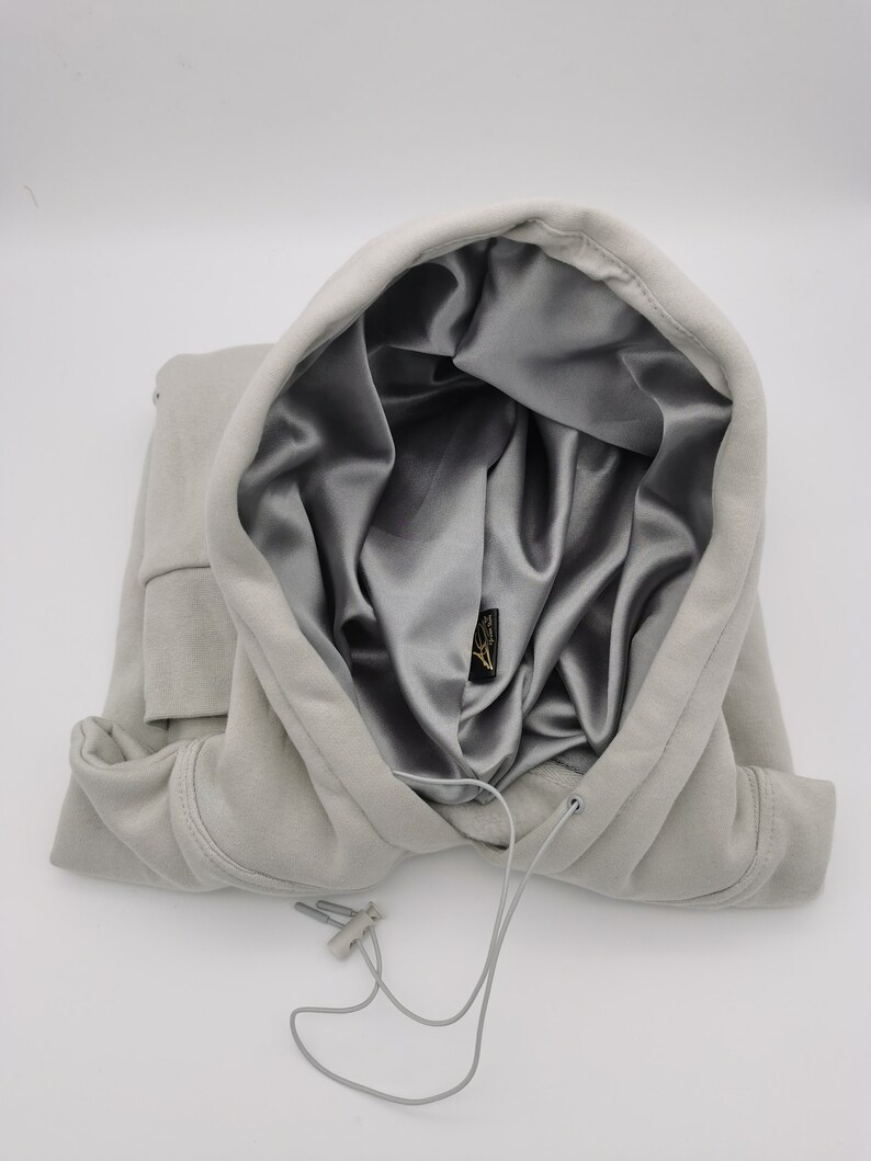 May include: A gray hooded sweatshirt with a silver satin lining. The hood is pulled up and the drawstring is visible.