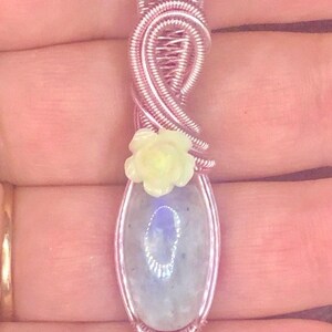 May include: A silver and rose gold wire wrapped pendant featuring a light blue oval gemstone and a yellow flower accent.