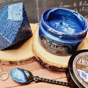 May include: A jar of blue opal jewel effect paste, with a small scoop of the paste on a spoon. The jar is labeled "Jewel Effect Paste Blue Opals".