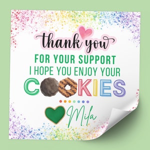 May include: A square card with a white background and colorful paint splatters. The text reads "thank you" above "FOR YOUR SUPPORT I HOPE YOU ENJOY YOUR COOKIES". Two cookie illustrations are included. The name "Mila" is written at the bottom.