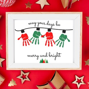 May include: A framed print featuring the text "may your days be merry and bright" with a graphic of four handprints in red and green hanging from a black string of lights. The handprints are stylized as light bulbs, with small triangles below.