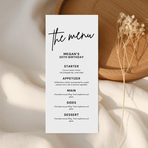 May include: A minimalist menu card with the words "the menu" in elegant script. The card lists a menu for Megan's 30th birthday, including starter, appetizer, main, sides, and dessert options. The card is white with black text.