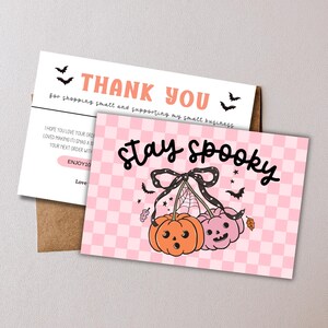 Pode incluir: Um conjunto de cartões de agradecimento com tema de Halloween. O cartão da frente apresenta a frase "Stay Spooky" com ilustrações de abóboras em um fundo xadrez rosa. O cartão que acompanha diz "Thank You" e inclui uma mensagem para pequenas empresas.