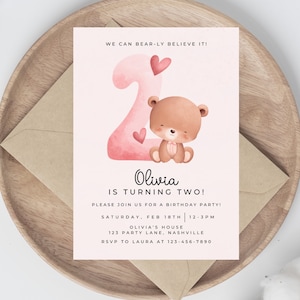 May include: Pink and white birthday invitation with a watercolor illustration of a teddy bear holding a heart. The invitation says "We can bear-ly believe it! Olivia is turning two!" and includes details for a birthday party.