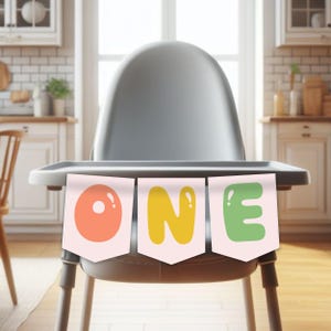 May include: A gray high chair with a banner that spells "ONE" in colorful letters. The banner has a peach-colored "O", a yellow "N", and a green "E". The high chair is in a kitchen setting.