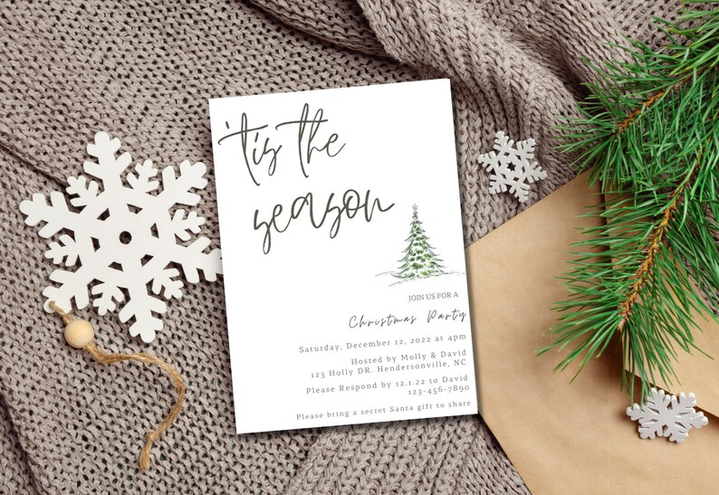 May include: A white card with the text 'Tis the season' in black cursive script. The card is decorated with a watercolor illustration of a green pine tree. The text below the illustration reads 'Join us for a Christmas Party' followed by details about the party, including the date, time, host, address, and RSVP information. The card is lying on a brown knitted blanket with a white snowflake ornament.