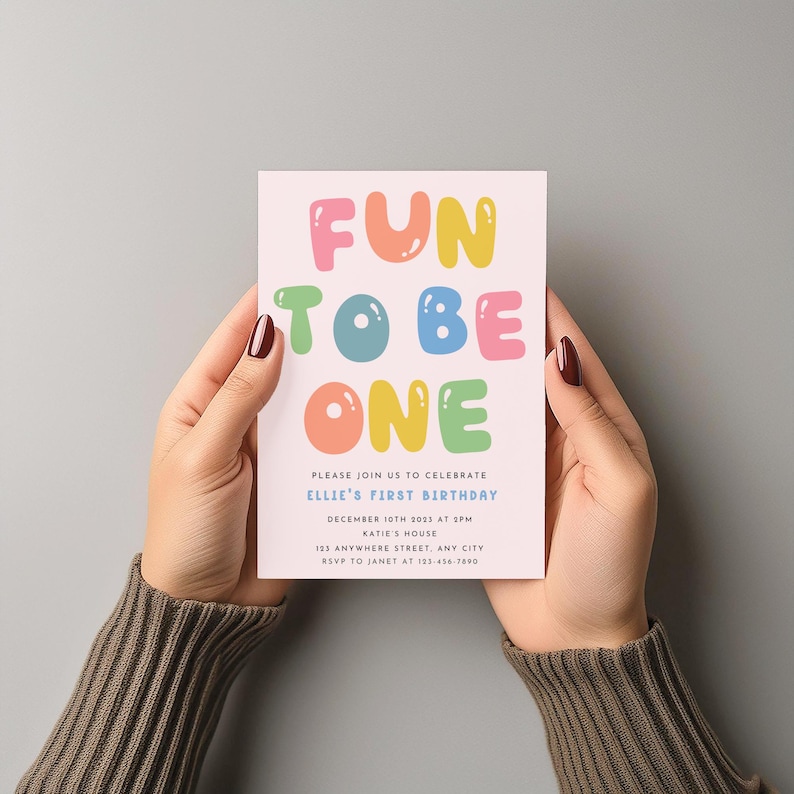 Może przedstawiać: R&oacute;żowe i białe zaproszenie na urodziny z tekstem "FUN TO BE ONE" w kolorowych literach w kształcie baniek. Zaproszenie zawiera informacje o pierwszym urodzinach Ellie, w tym datę, godzinę, miejsce i dane kontaktowe do RSVP.
