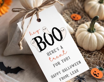 Op de afbeelding: Een wit cadeaulabel met het woord "BOO" in zwart, met illustraties van geesten en de tekst "Here's a treat for you! Happy Halloween". Het label is met touw aan een beige zakje bevestigd.