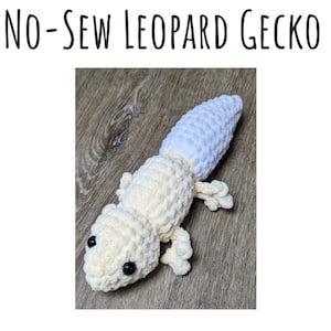 May include: A crocheted white and cream leopard gecko plush toy. The toy has black eyes and a white tail.
