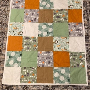 May include: A patchwork quilt with a variety of woodland animal and nature-themed prints. The quilt is made up of squares in shades of green, brown, orange, and white.
