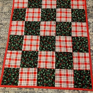 May include: A red and white plaid and green holly patterned quilt with a red border.