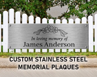 May include: A rectangular brushed stainless steel memorial plaque featuring four corner mounting bolts. The centre is engraved with a floral motif above the text In loving memory of James Anderson in a black serif font.