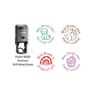May include: A black and grey Trodat 46025 premium self-inking stamp. Four circular stamp impressions are shown: a green puppy with 'Miss Brown says Grrreat work!', a brown cookie with 'Miss Brown says Smart cookie!', a red rainbow with 'Miss Brown is proud of you', and a purple cupcake with 'Miss Brown says Sweet success'.