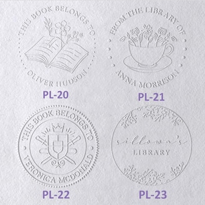 May include: Four circular embossed book embosser designs on white paper. PL-20 features an open book with flowers and the text 'THIS BOOK BELONGS TO OLIVER HUDSON'. PL-21 shows a teacup with flowers and 'FROM THE LIBRARY OF ANNA MORRISON'. PL-22 displays a shield and swords with 'THIS BOOK BELONGS TO VERONICA MCDONALD'. PL-23 shows floral borders with 'sillowa's LIBRARY'.