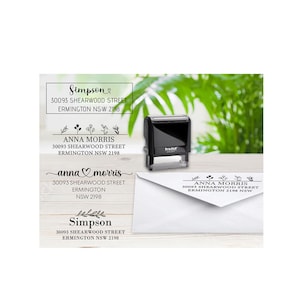 May include: A black self-inking rubber stamp positioned next to a white envelope. The stamp and envelope display printed return address text including the names Simpson and Anna Morris, along with the address 30093 Shearwood Street, Ermington NSW 2198.