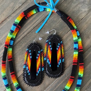 May include: A beaded necklace and earrings set with a black, orange, yellow, green, and blue geometric pattern. The necklace is made of black beads with colorful accents. The earrings are long and dangle, with a black background and colorful geometric designs.