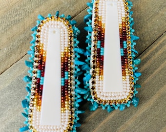 May include: A pair of white bone earrings with turquoise, red, and gold beadwork.