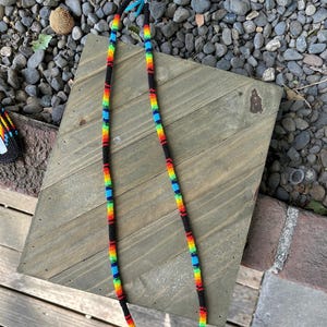 May include: A beaded lanyard with a rainbow pattern and black accents. The lanyard is made of small, colorful beads and is approximately 30 inches long.