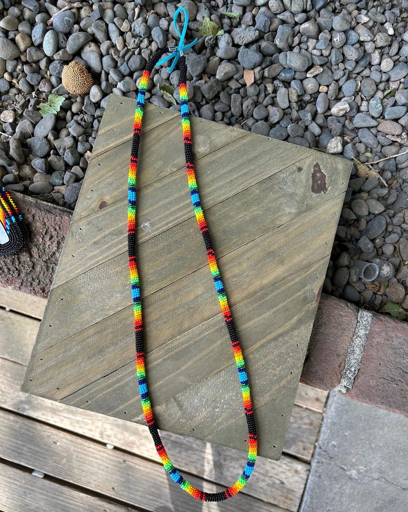 May include: A beaded lanyard with a rainbow pattern and black accents. The lanyard is made of small, colorful beads and is approximately 30 inches long.