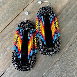 May include: A pair of black beaded earrings with colorful geometric patterns. The earrings are oval shaped and have a black backing.