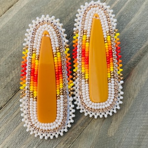 May include: A pair of beaded hair clips with a yellow, orange, and red design. The clips are made with white beads and gold accents.