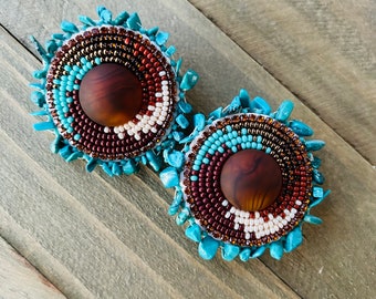 May include: A pair of large, round earrings with a brown center and turquoise and white beading around the edge.