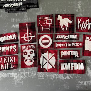 May include: A collection of red and black plaid patches featuring white text and graphics. The patches display band names like "Korn," "Misfits," and "Black Flag," along with other logos and text.
