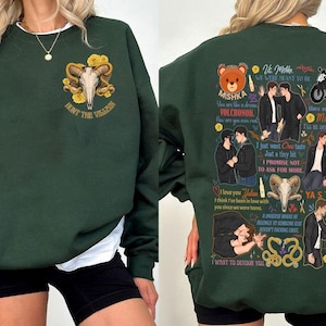 May include: Dark green sweatshirt with a white crew neck. The front features a skull with horns and the text "HUNT THE VILLAIN". The back has illustrations and text including "Mishka", "I love you Julian", and "YA S TOBOY".