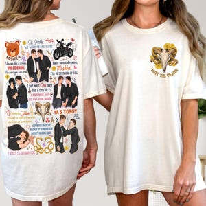 May include: Cream-colored t-shirt with various graphic designs. The front features a skull with horns and the text "HUNT THE VILLAIN." The back displays multiple illustrations of two men, along with text and symbols.