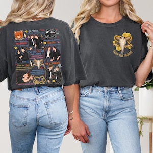 May include: Dark gray t-shirts with graphic designs. One shirt features a bear, text, and illustrations. The other shirt displays a skull with yellow roses and the text "HUNT THE VILLAIN".