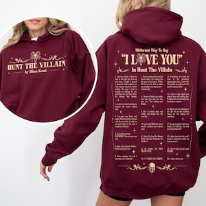 May include: Burgundy hoodie with the text "HUNT THE VILLAIN" and "by Rina Kent" in a gold font. The back of the hoodie has the text "Different Way To Say 'I LOVE YOU' In Hunt The Villain" with a list of phrases in gold.