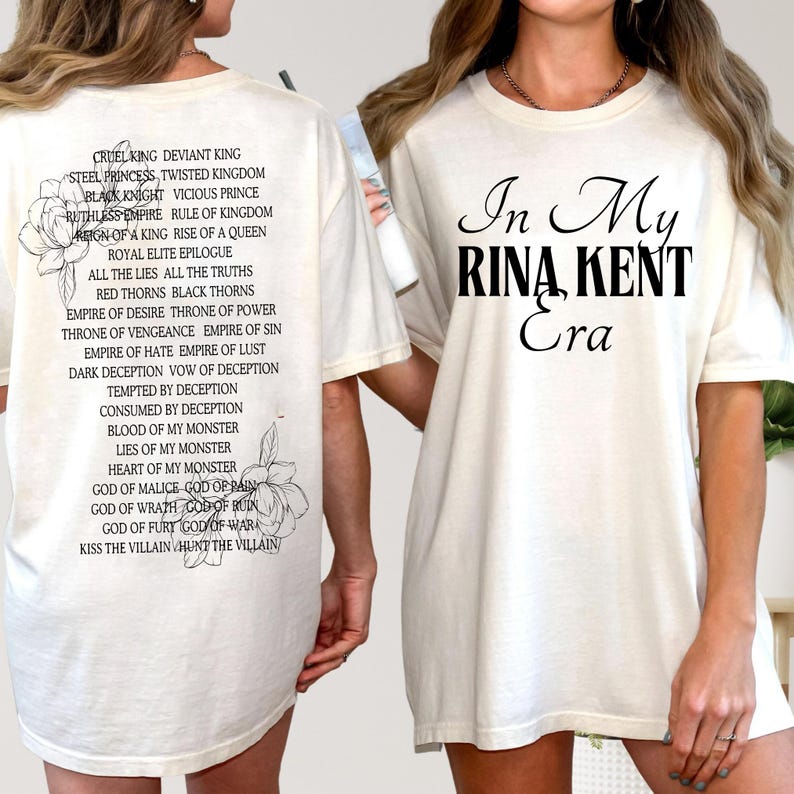 May include: Cream-colored t-shirt with black text that reads "In My Rina Kent Era" on the front. The back of the shirt features a list of phrases and flower illustrations. A casual, comfortable tee.