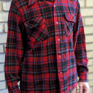 May include: A red, black, and blue plaid flannel shirt with a button-down collar and two chest pockets.
